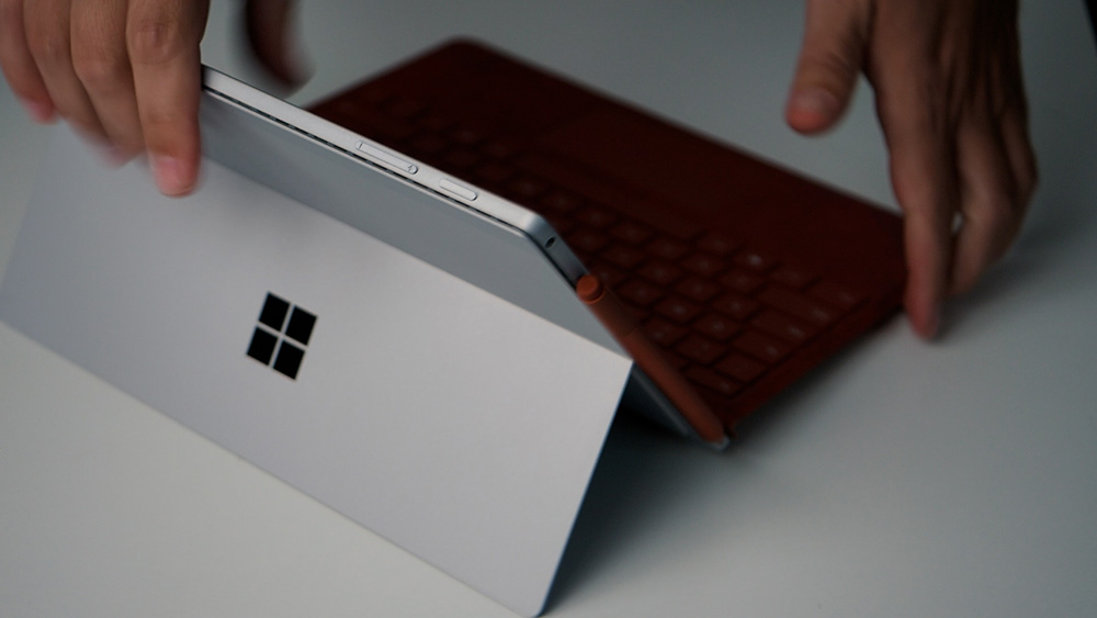 The new unboxed Surface Pro 7+ on the desk with the poppy red keyboard and poppy red Surface pen attached.